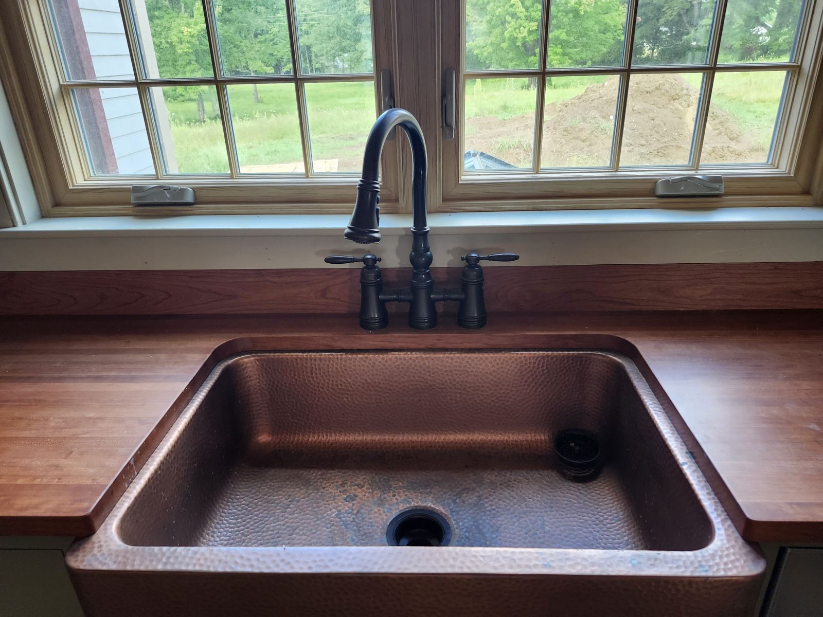 Hammered copper farmhouse sink with oil-rubbed bronze bridge faucet on a butcher block counter